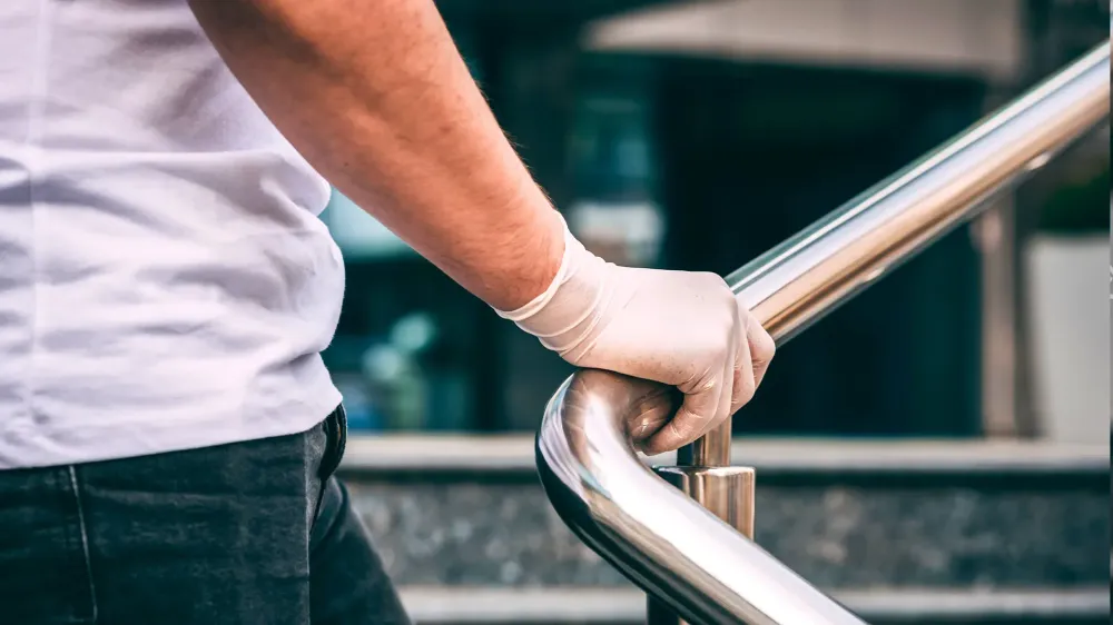 Male hand in a white latex medical glove on the railing. man wearing protective latex gloves touching railing outside